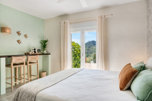 A bedroom with a bed, a desk with two chairs, a window with curtains, and a view of greenery outside. - Room 'Menta' with Mountain View, Wi-Fi and Air Conditioning (L'Atzúbia)