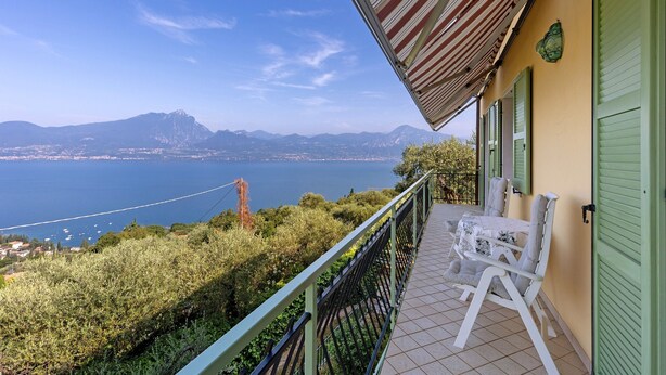 Un balcón con vistas al mar y a las montañas, una mesa con sillas y una puerta verde.