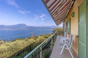 Un balcón con vistas al mar y a las montañas, una mesa con sillas y una puerta verde.