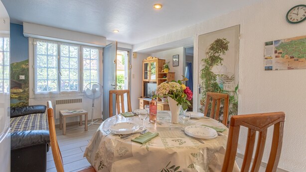 Un coin repas avec une table ronde dressée pour quatre personnes, un vase rempli de fleurs et une horloge au mur.