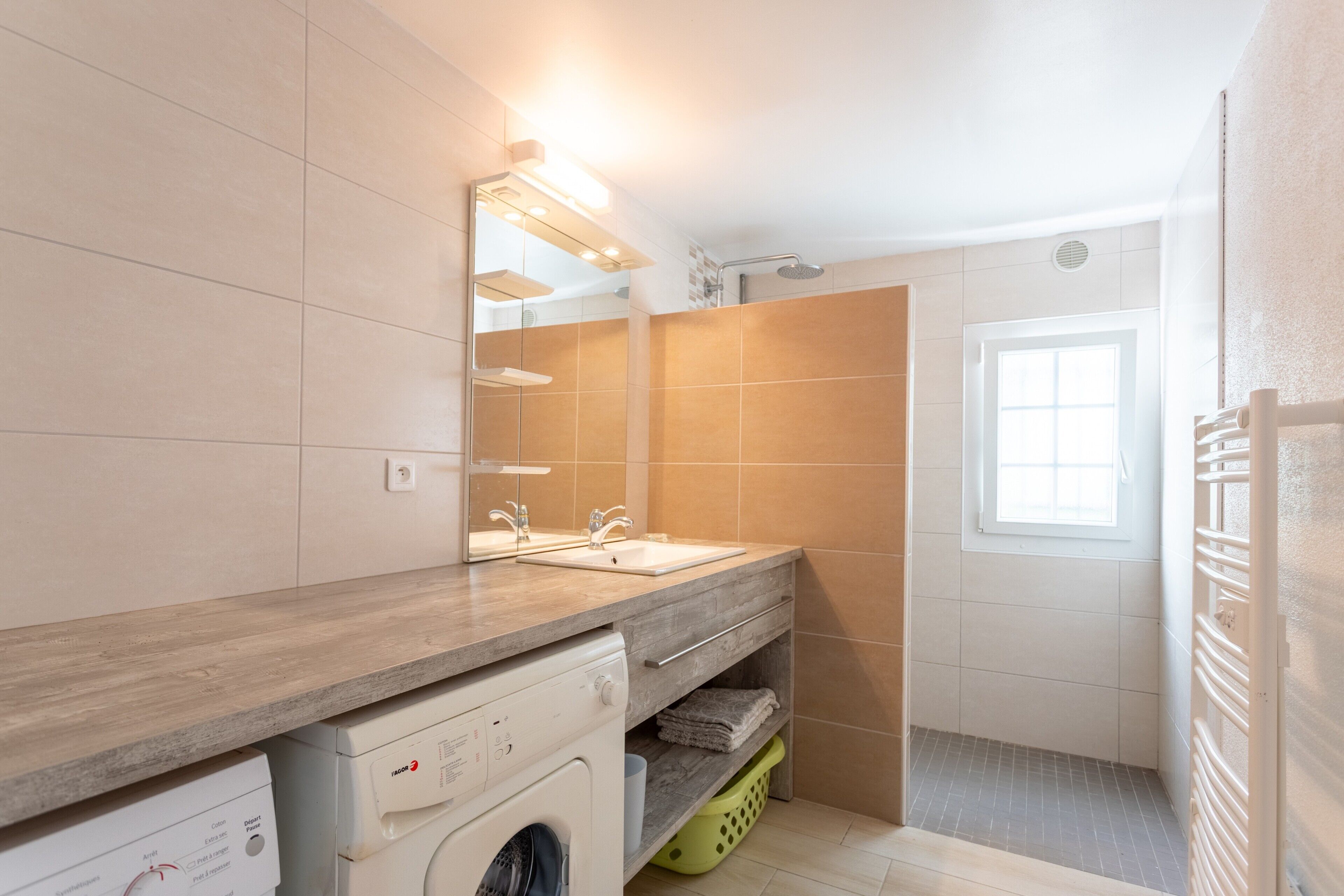 Une salle de bain moderne avec un meuble-lavabo en bois, deux vasques, un lave-linge encastré et un espace douche.