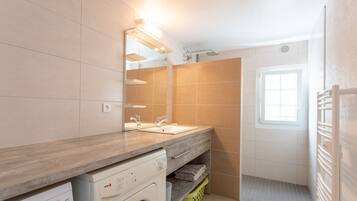 Une salle de bain moderne avec un meuble-lavabo en bois, deux vasques, un lave-linge encastré et un espace douche.