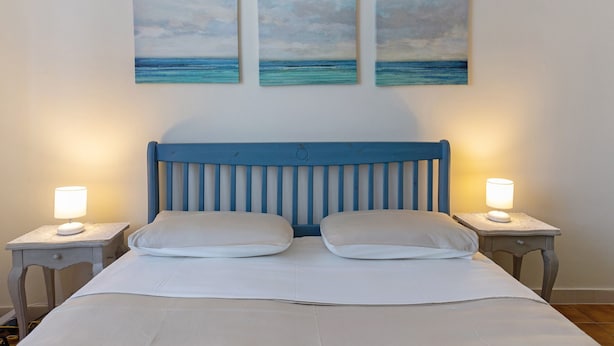 A bed with a blue headboard, two bedside lamps, and three paintings of the ocean on the wall.