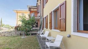 A row of white lounge chairs outside a building with a stone pathway, a small tree, and a stone wall.