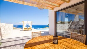 Een houten tafel met stoelen en een hanglamp op een balkon met uitzicht op zee.