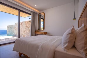 Ein Schlafzimmer mit einem großen Bett, einem Nachttisch aus Holz, einem Spiegel und Meerblick.