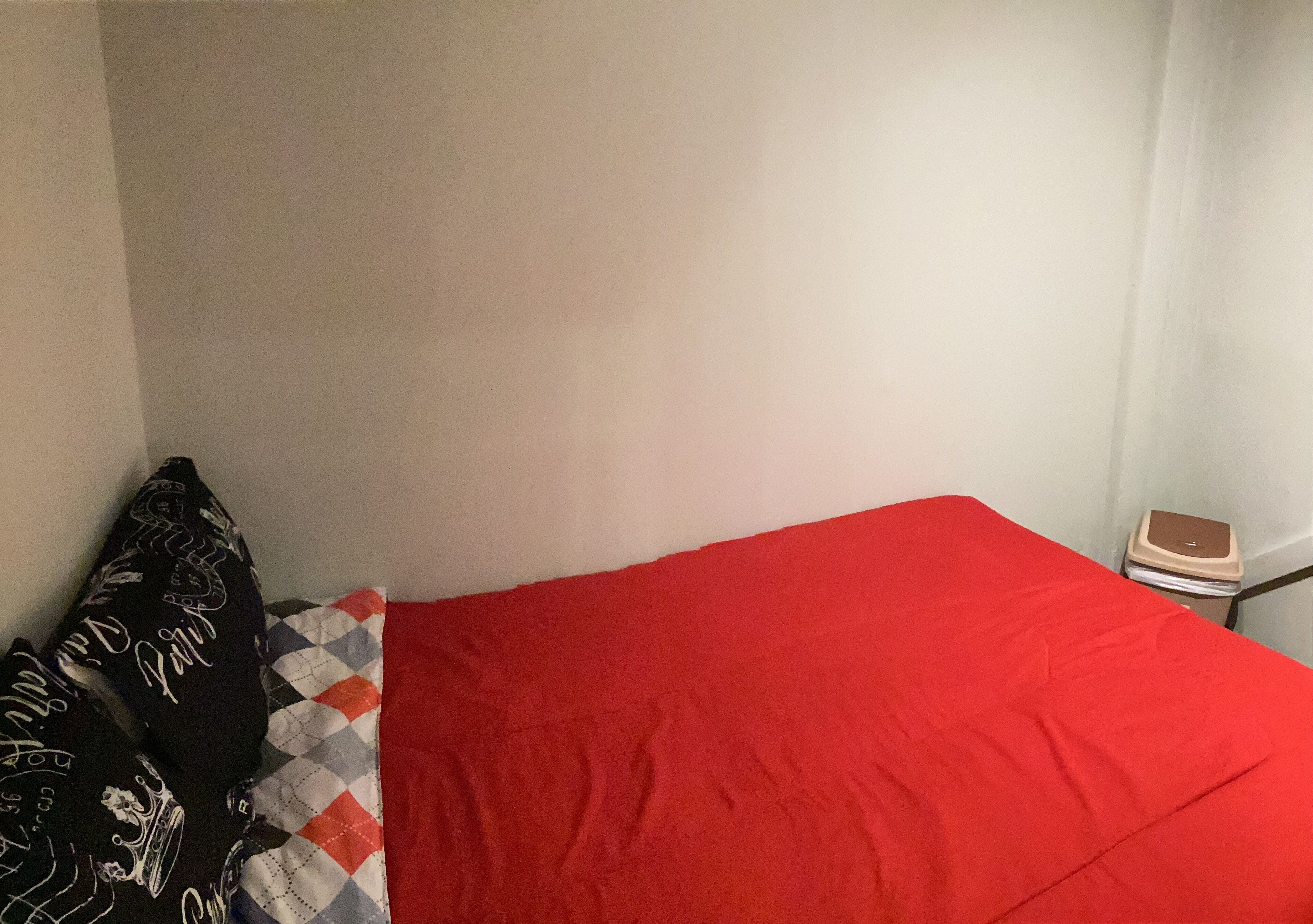Ein Bett mit einer roten Decke, einem schwarzen Kissen mit weißen Mustern und einem kleinen Nachttisch mit einer Waage.