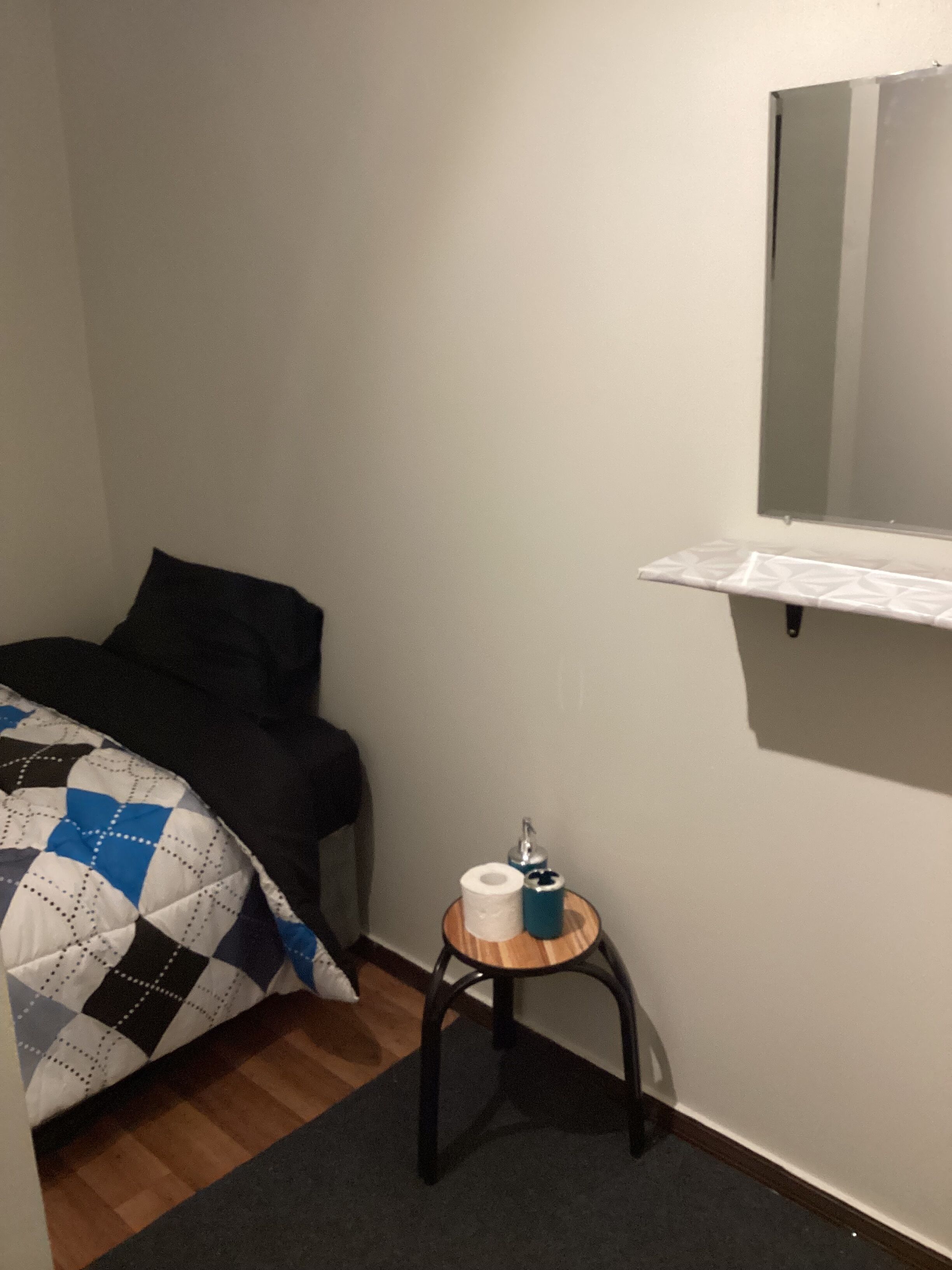 Ein Schlafzimmer mit einem Bett, einem kleinen Nachttisch mit Lampe, einem Spiegel und einem Regal.