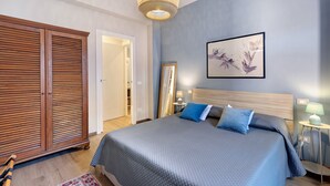 Ein Schlafzimmer mit Bett, Schrank, Spiegel, Wandbild und Nachttisch mit Lampe.