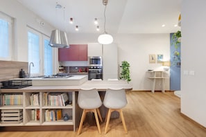 A modern kitchen with a central island, built-in bookshelves, and a dining area with two chairs.