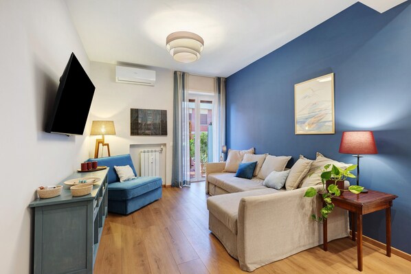 A modern living room with a blue accent wall, a flat-screen TV, a sofa, a coffee table, and a side table with a plant.