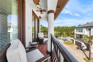 A balcony with wicker furniture, a ceiling fan, and a view of a swimming pool and neighboring houses.