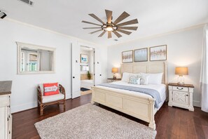 A bedroom with a bed, bedside tables, a ceiling fan, a mirror, and a door leading to a bathroom.