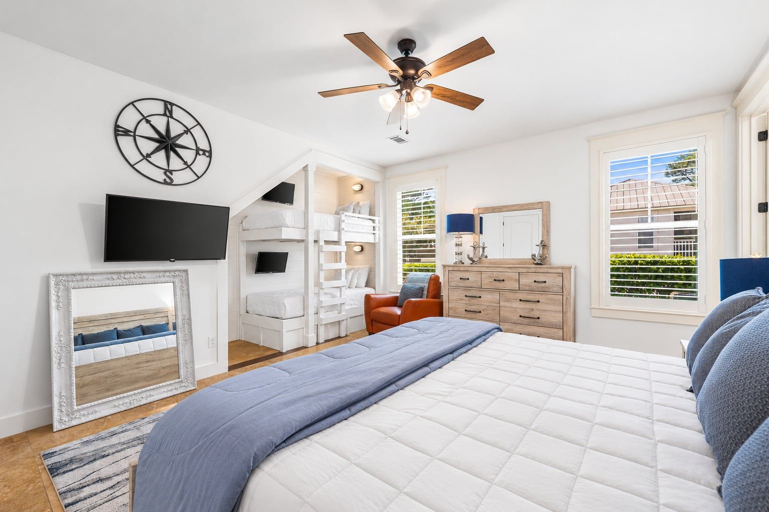 A bedroom with a bed, a TV, a ceiling fan, a dresser, a mirror, and a window with blinds.