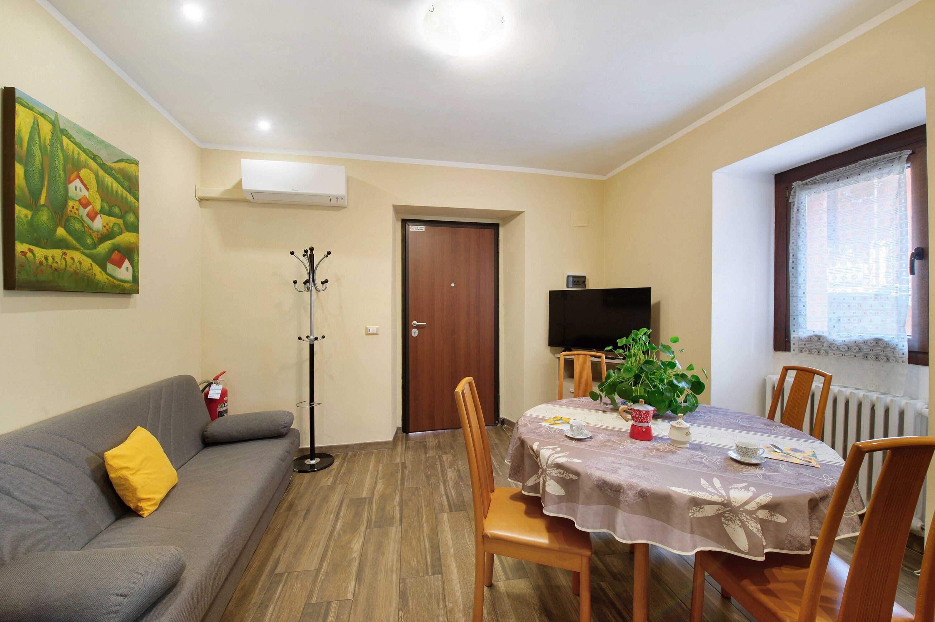 Ein Wohnzimmer mit einer Couch, einem Esstisch mit Stühlen, einem Fernseher und einem Bild an der Wand.