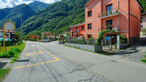 Una strada con una fermata dell'autobus, un edificio con balconi e montagne sullo sfondo.