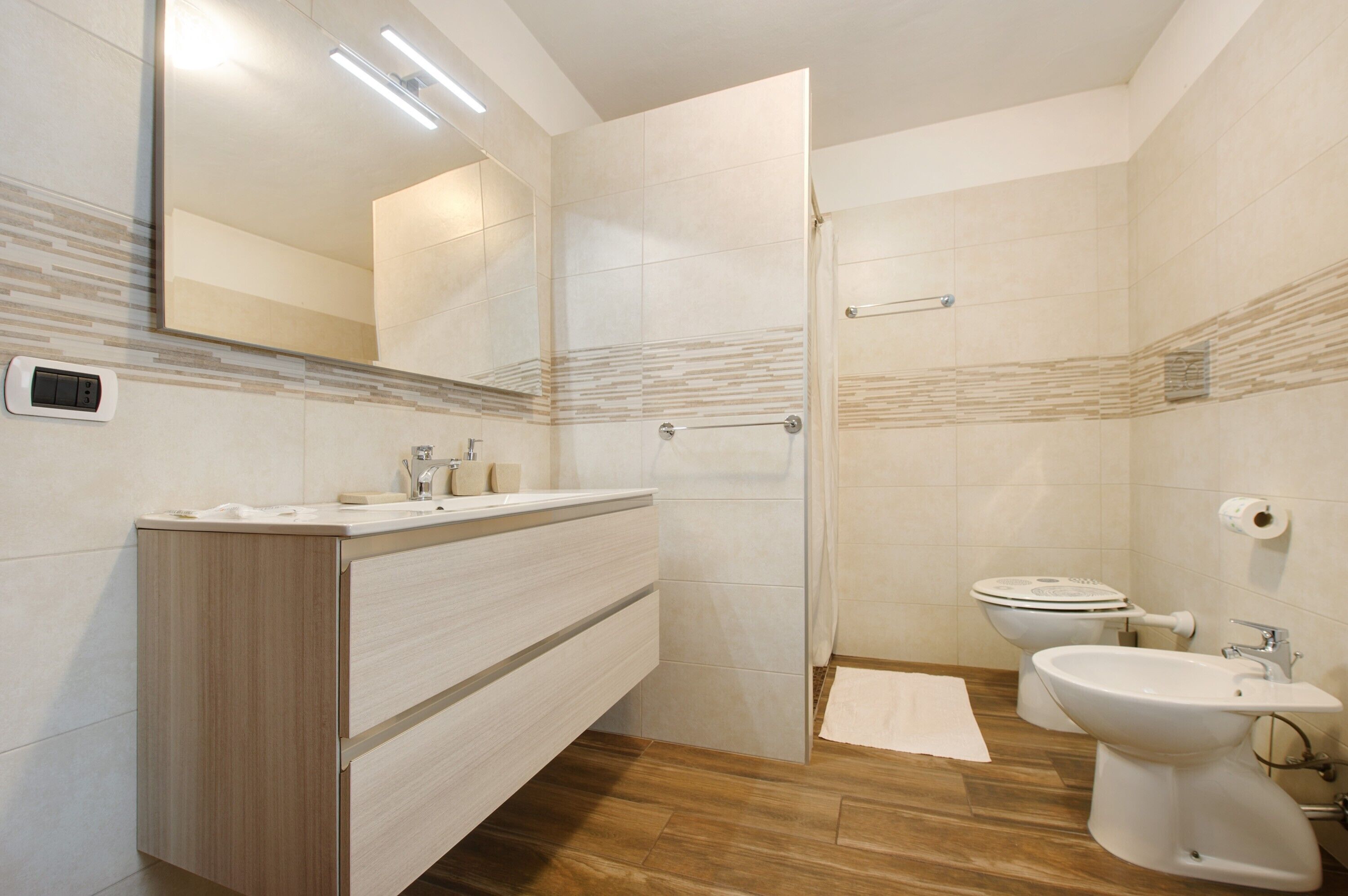 A modern bathroom with a wooden vanity, a shower, a toilet, and a bidet.
