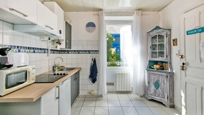 Une cuisine avec des meubles blancs, un four à micro-ondes, un évier et une fenêtre donnant sur l’extérieur.