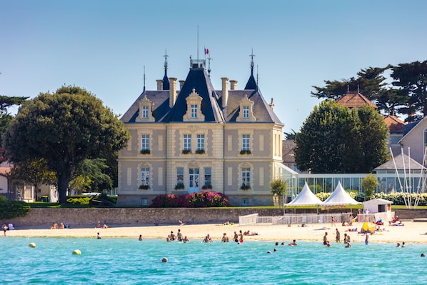 Un grand bâtiment doté d’une tour imposante, situé au bord de l’eau, avec une plage où se trouvent des gens.