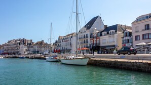 Un port où des bateaux sont amarrés, des bâtiments le long de la rive et une promenade pavée.