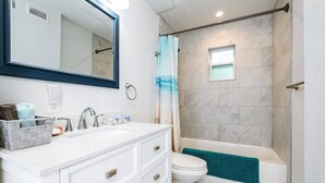 A bathroom with a white vanity, a large mirror, a toilet, and a shower area with a blue towel. - Newly Updated Walk to Beach & Ocean Center (Daytona Beach)