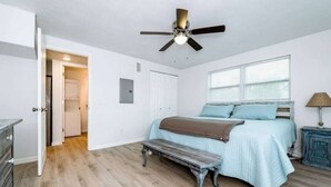 Un dormitorio con cama, una banca, ventilador de techo, ventana y puerta.