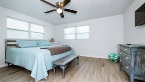 Une chambre à coucher avec un lit, un banc, une commode et un ventilateur de plafond.