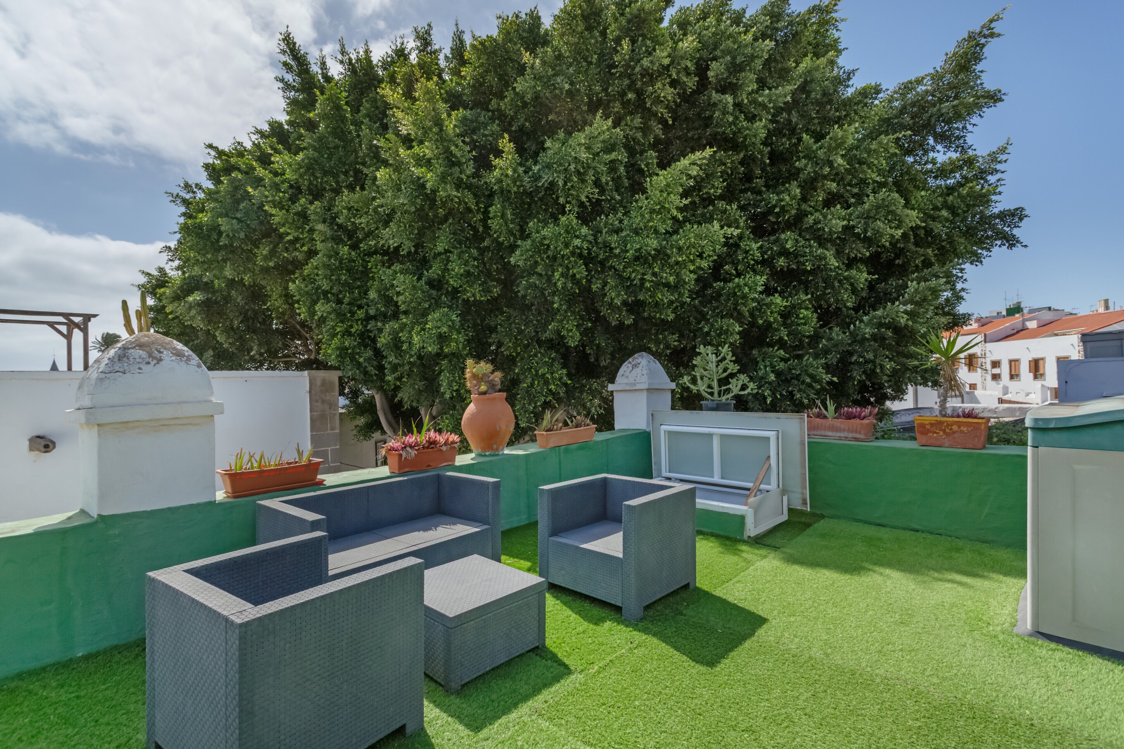 Eine Terrasse im Freien mit Korbmöbeln, künstlichem Rasen und Topfpflanzen.