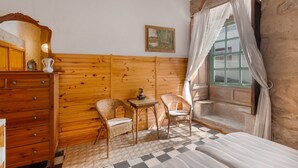 A room with wooden panel walls, a bed, two wicker chairs, a small table, a dresser, and a window with curtains. - Holiday Home 'San Francisco 1' with Mountain View, Private Terrace and Wi-Fi (Telde)