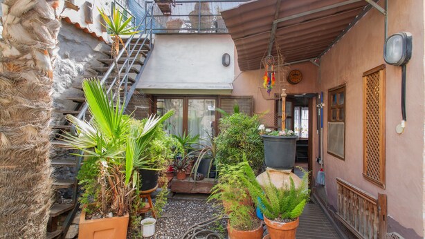 A narrow alley with potted plants, a staircase, and a building with a balcony.