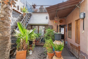 Une ruelle étroite bordée de plantes en pot, un escalier et un immeuble doté d’un balcon.