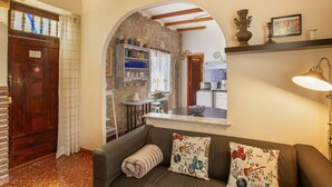 A cozy living area with a sofa, a kitchen visible through an archway, and a wooden door.