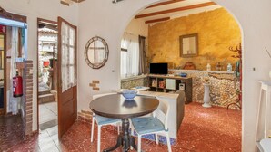 A dining area with a round table and chairs, a kitchen with a tiled backsplash, and an arched doorway leading to another room.