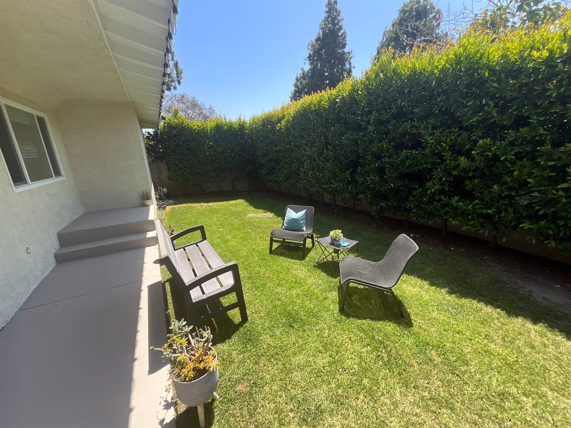 Un jardin avec une terrasse, deux chaises, une petite table et un pot de fleurs.