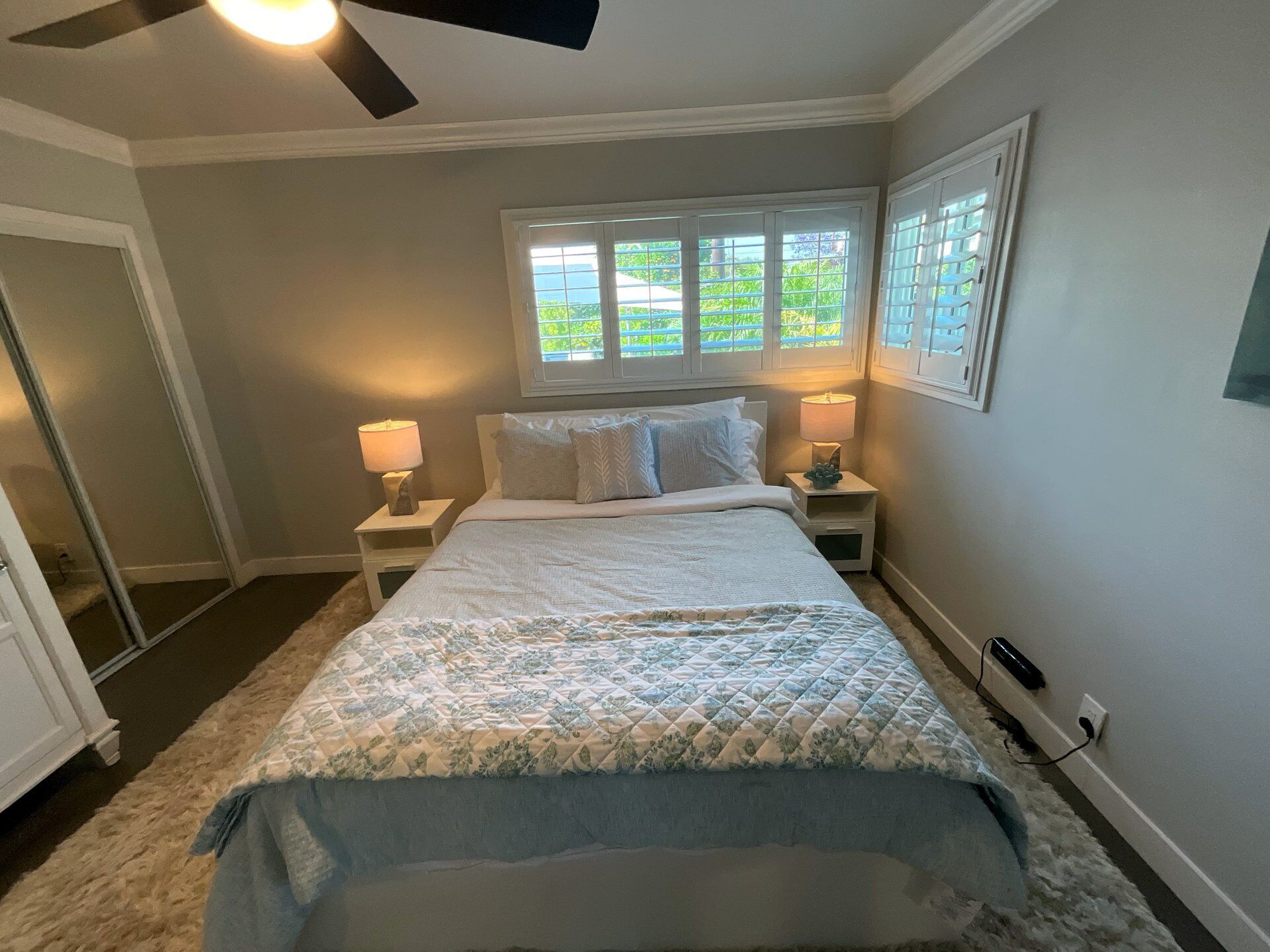 A bedroom with a bed, two bedside lamps, a window with blinds, and a ceiling fan.