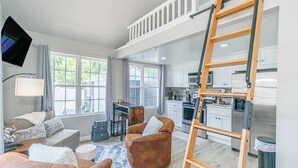 A spacious living area with a high ceiling, a kitchen with modern appliances, and a loft bedroom with a wooden ladder. - 148 Rockdale Street Tiny House (Myrtle Beach)