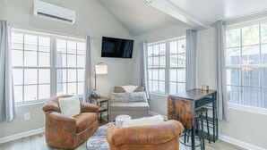 A living room with a sofa, ottoman, and a TV mounted on the wall. - 148 Rockdale Street Tiny House (Myrtle Beach)