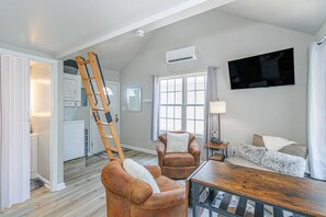 A living room with a loft bed, a wooden ladder, a television, and a fireplace. - 148 Rockdale Street Tiny House (Myrtle Beach)