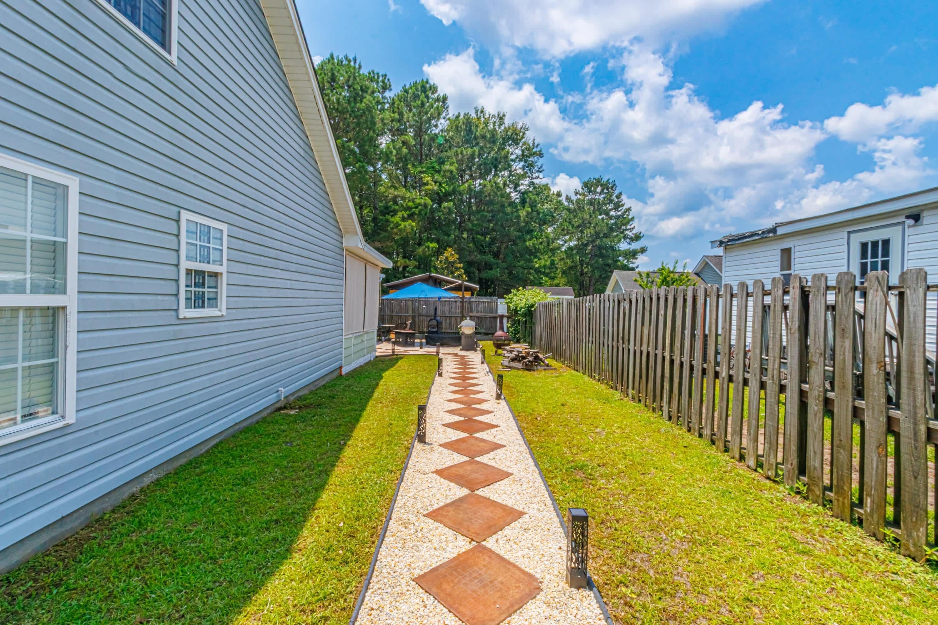 A backyard with a paved walkway, wooden fence, and a blue-roofed structure.