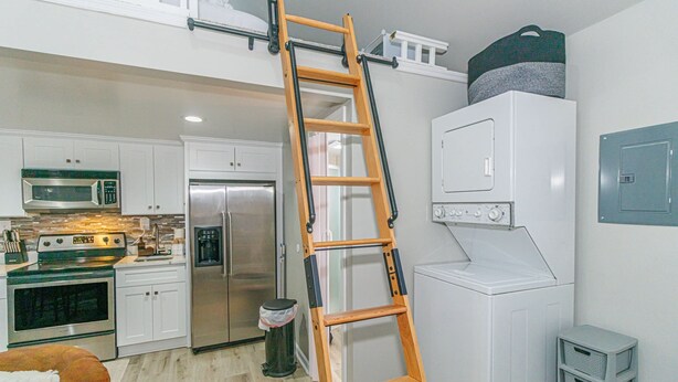A kitchen with white cabinets, a stainless steel refrigerator, a microwave, and a stove. - 148 Rockdale Street Tiny House (Myrtle Beach)