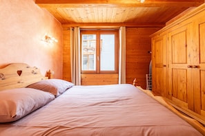 Quarto de cabana de madeira com cama, cortinas, janela e armários de madeira.