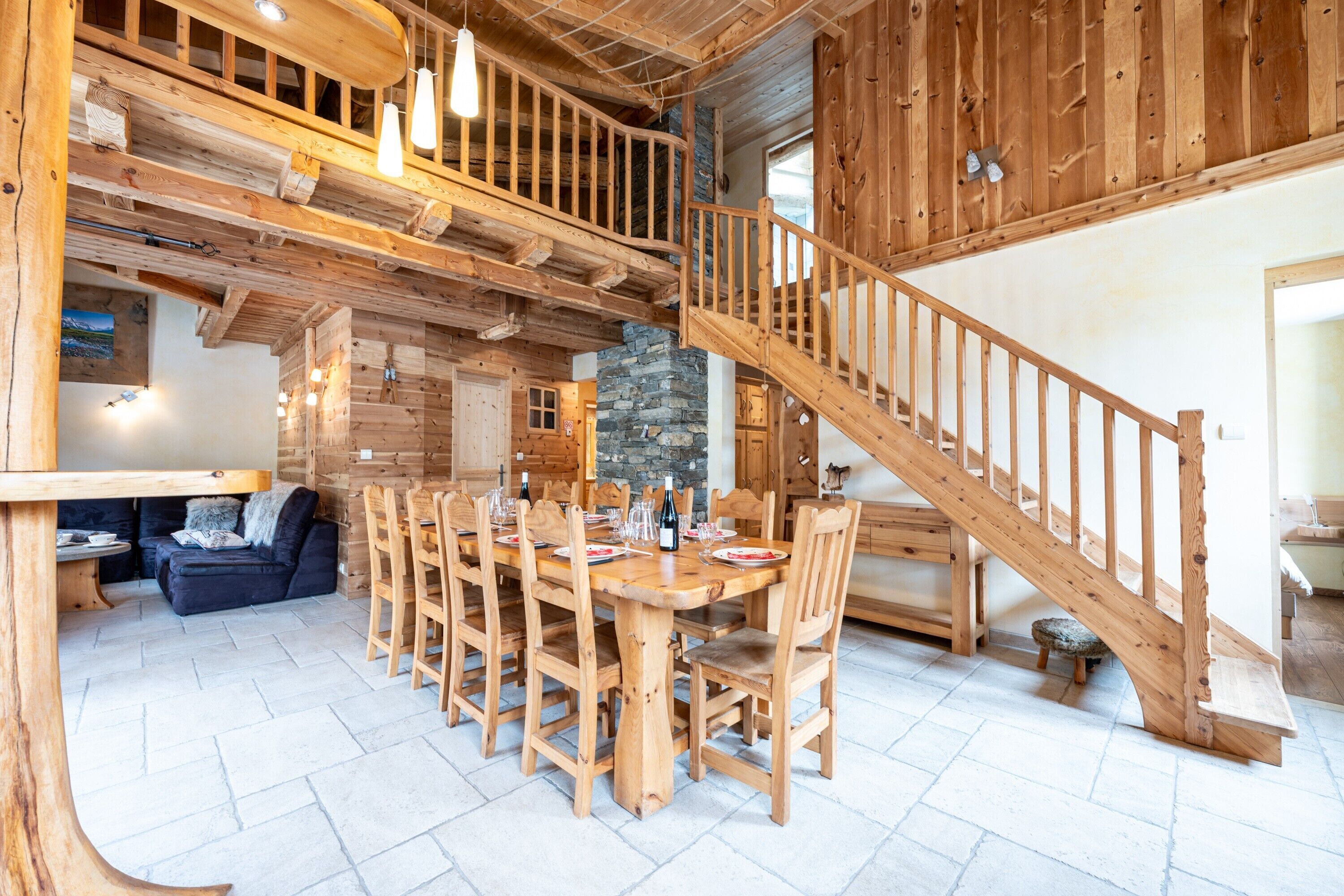 A wooden interior with a dining area, staircase, and stone pillar.
