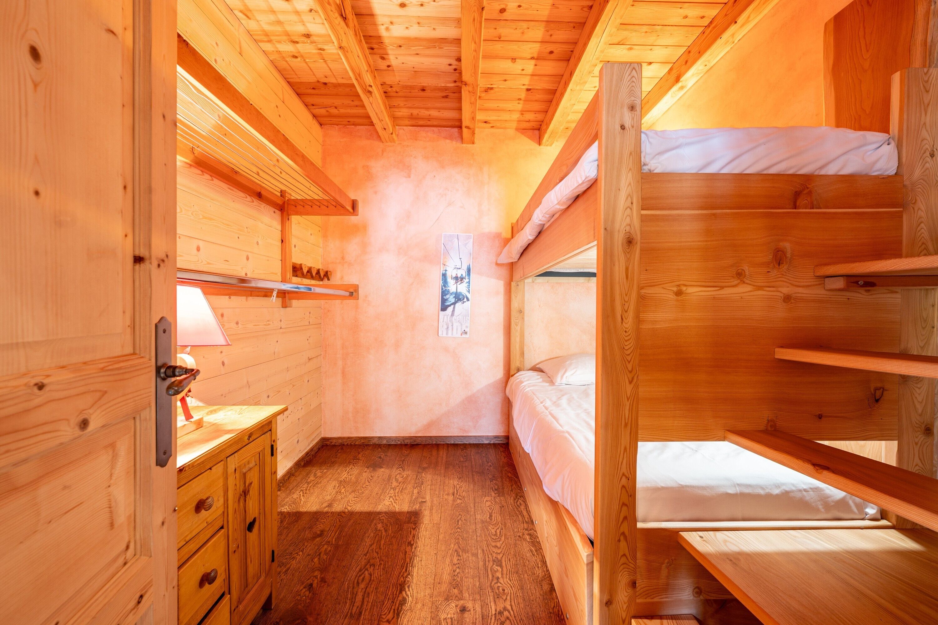 Ein Zimmer mit einem Holzbett mit Etagen, einer Holzkommode und einem gerahmten Bild an der Wand.
