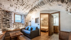 Una habitación acogedora con pared de piedra, un banco de madera, un sofá y una cama.
