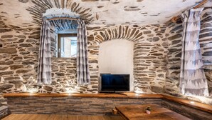 Una habitación con paredes de piedra, un televisor, un banco de madera y una pequeña mesa con una planta.