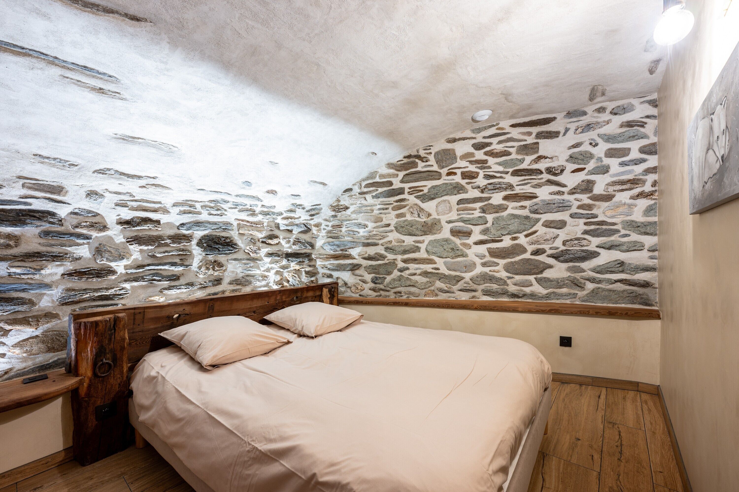 A bedroom with a stone wall, wooden headboard, and a bed with a beige bedspread.