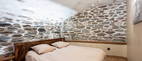 A bedroom with a stone wall, wooden headboard, and a bed with a beige bedspread.