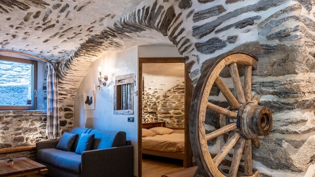 Una habitación acogedora con paredes de piedra, una rueda de madera, un sofá y una cama.