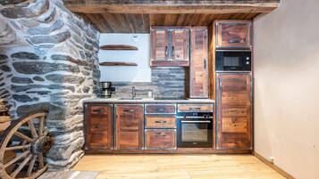 A rustic kitchen with wooden cabinets, a stone wall, and a wooden ceiling.