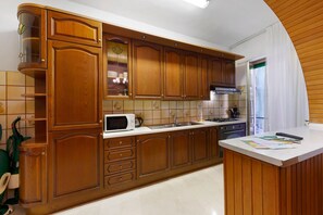 Une cuisine avec des meubles en bois, un four à micro-ondes, un évier et un plan de travail recouvert de papiers.
